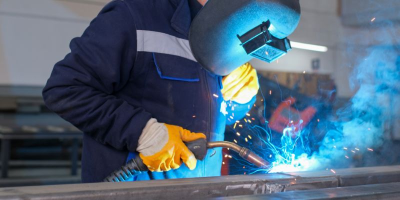 A person in a welding mask using a MIG welder on a piece of metal.